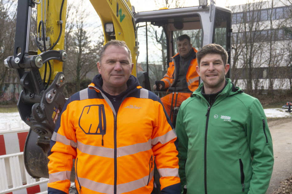 Zwei Männer stehen vor einem E-Bagger. Einer trägt eine Nibler-Jacke, der andere eine von Wacker Neuson. E-Bagger EZ26e im Einsatz auf der Grünen Baustelle